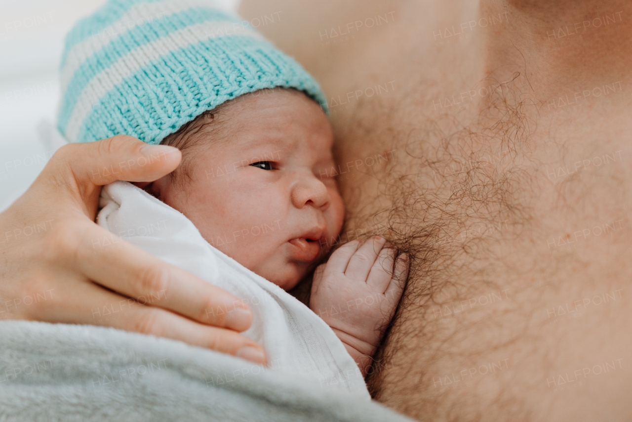 Proud father bonding with newborn baby right after birth. Holding baby for the first time. Skin to skin contact.