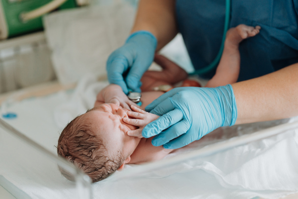 Neonatal nurse, doctor examining newborn baby, listening to heartbeat with stethoscope. Taking care of infant after birth.Neonatal care, newborn's health and well-being.