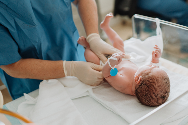 Neonatal nursers, doctor examining newborn baby, putting diaper on, taking care of infant after birth. Neonatal care, newborn's health and well-being.