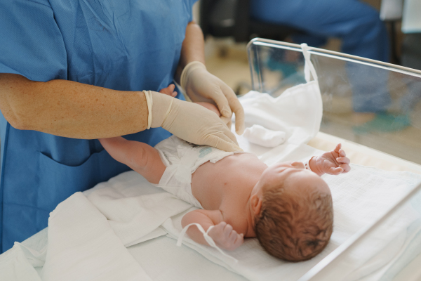 Neonatal nursers, doctor examining newborn baby, putting diaper on, taking care of infant after birth. Neonatal care, newborn's health and well-being.