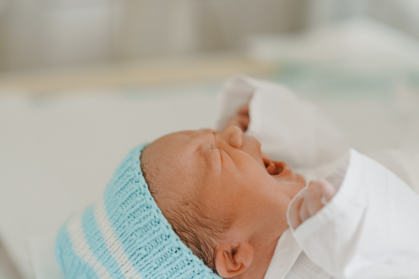 Portrait of newborn baby crying. Taking care of infant after birth. Neonatal care, newborn's health and well-being.