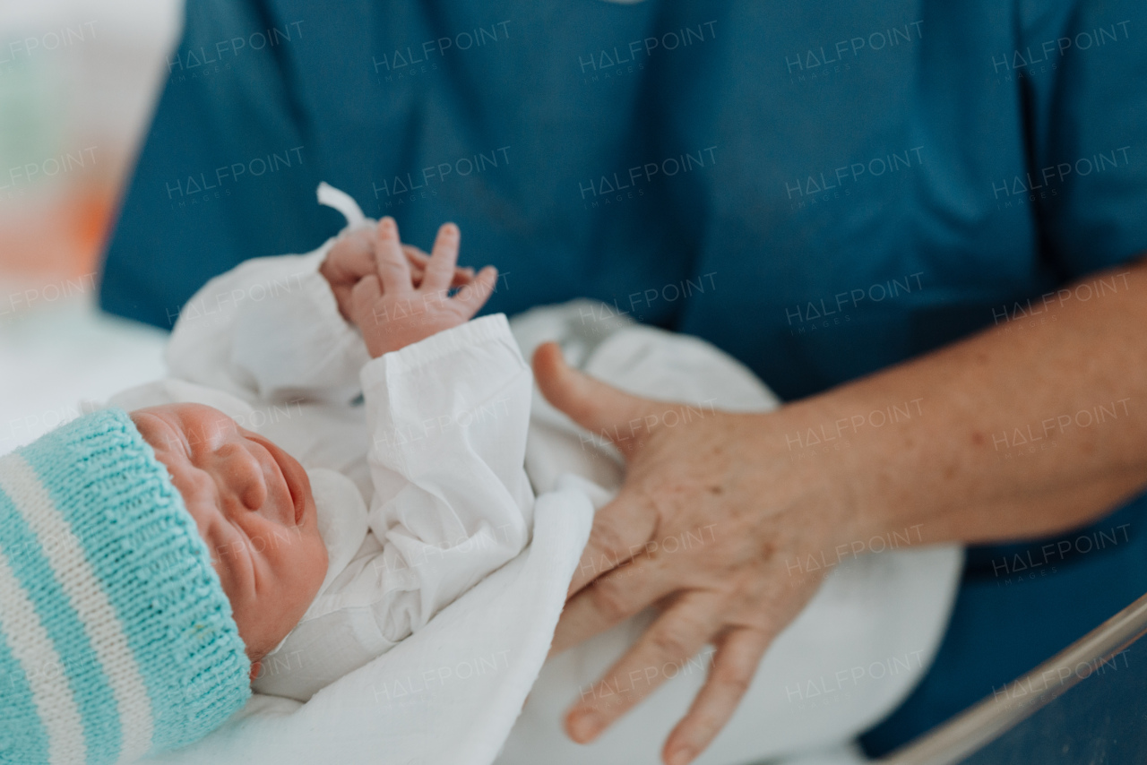 Obstetrician or neonatologist doctor holding newborn baby. Doctor examining, taking care of infant after birth. Neonatal care, newborn's health and well-being.