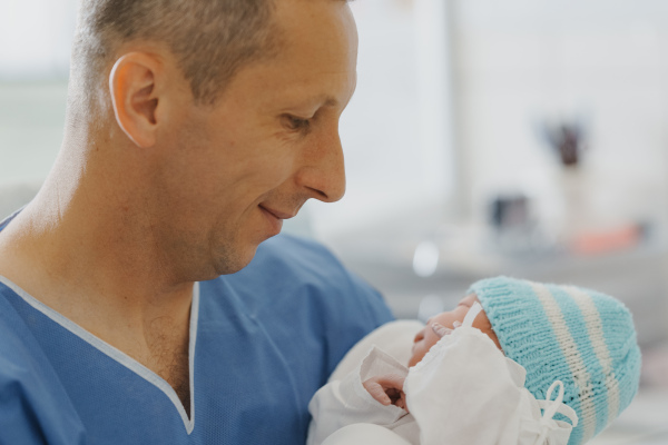 Male obstetrician or neonatologist doctor holding newborn baby. Doctor examining, taking care of infant after birth. Neonatal care, newborn's health and well-being.