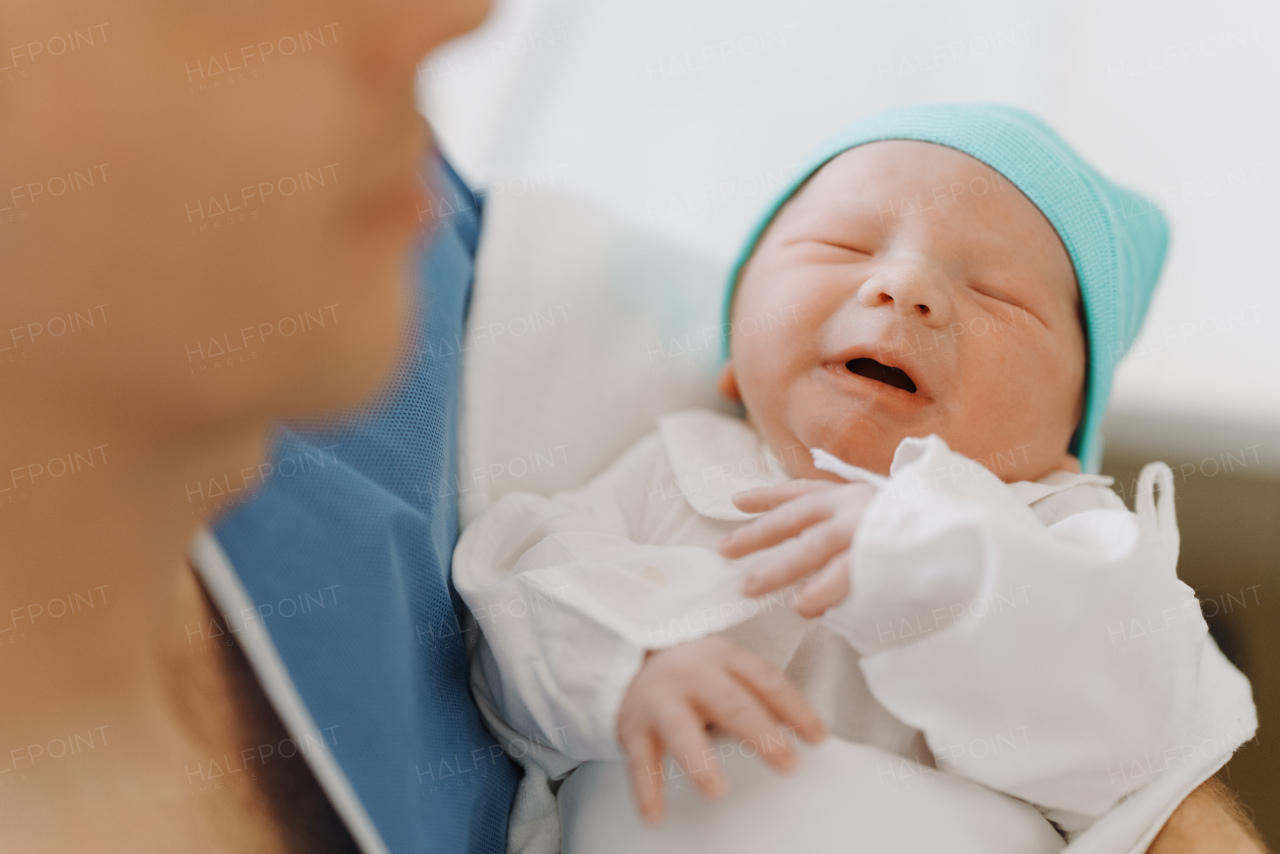 Male obstetrician or neonatologist doctor holding newborn baby. Doctor examining, taking care of infant after birth. Neonatal care, newborn's health and well-being.