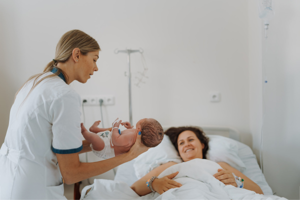 Lactation consultant helping with breastfeeding newborn baby, latching, feeding on first milk, colostrum. Happy mother bonding with newborn baby right after birth. Skin to skin contact.