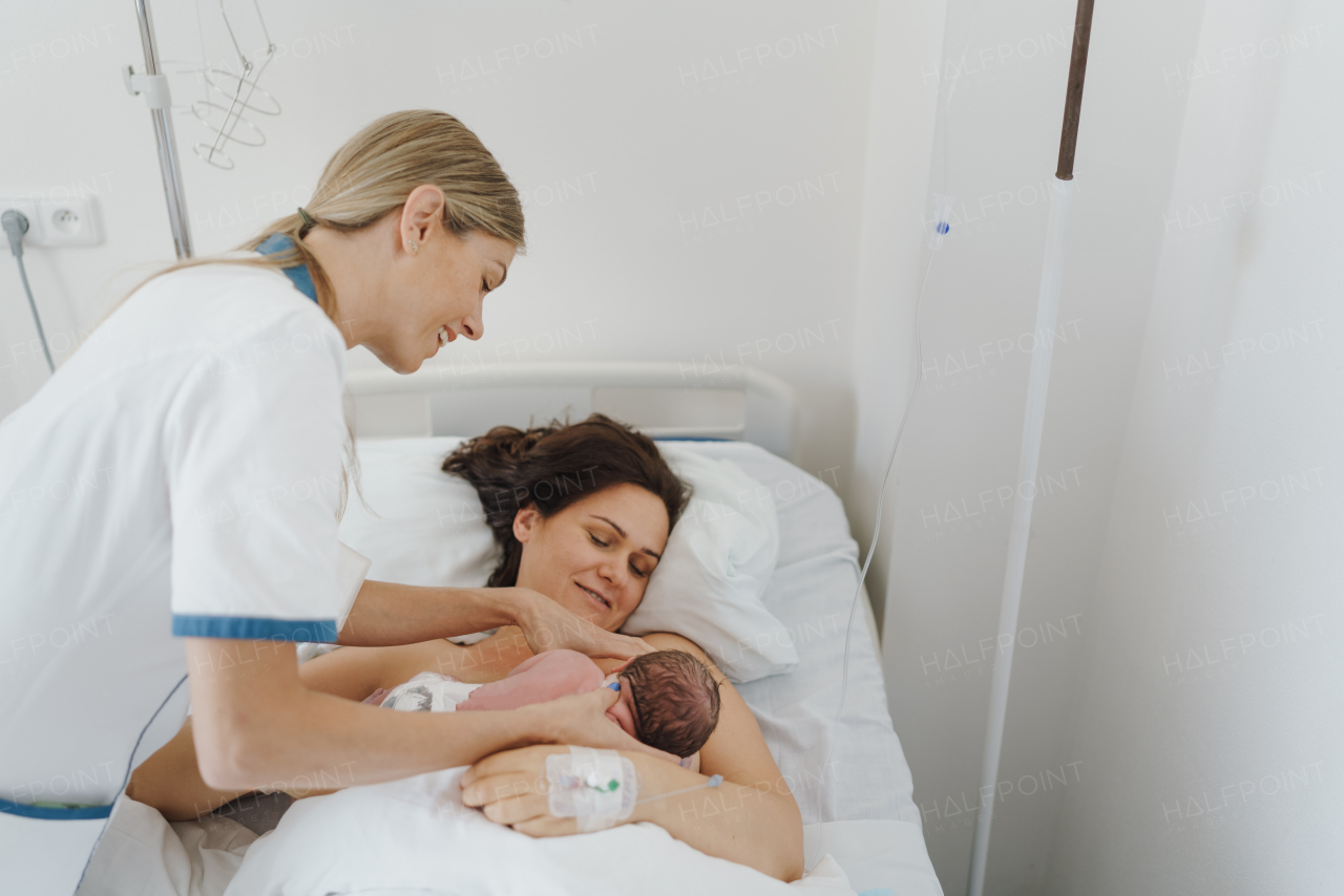 Lactation consultant helping with breastfeeding newborn baby, latching, feeding on first milk, colostrum. Happy mother bonding with newborn baby right after birth. Skin to skin contact.