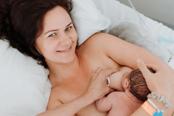 Breastfeeding newborn baby, latching, feeding on first milk, colostrum. Happy mother bonding with newborn baby right after birth. Skin to skin contact.