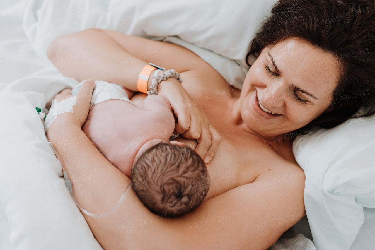 Breastfeeding newborn baby, latching, feeding on first milk, colostrum. Happy mother bonding with newborn baby right after birth. Skin to skin contact.