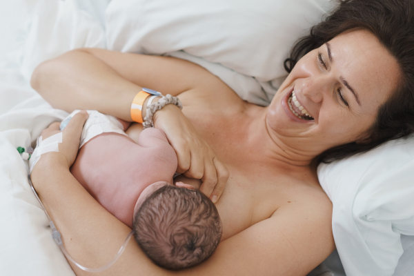 Happy mother bonding with newborn baby right after birth, first latching, breastfeeding. Skin to skin contact.