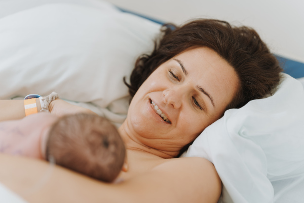 Breastfeeding newborn baby, latching, feeding on first milk, colostrum. Happy mother bonding with newborn baby right after birth. Skin to skin contact.