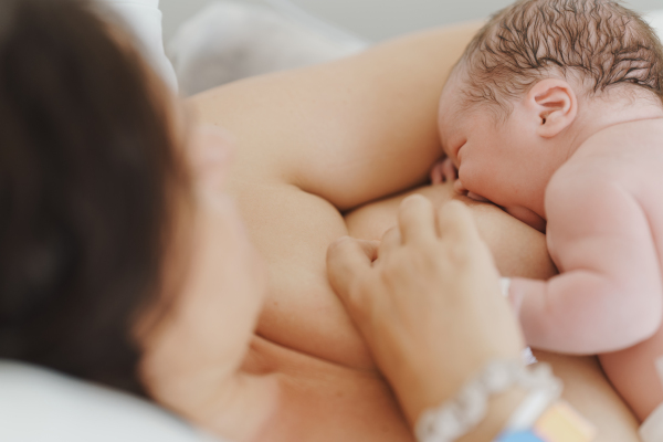 Breastfeeding newborn baby, latching, feeding on first milk, colostrum. Happy mother bonding with newborn baby right after birth. Skin to skin contact.