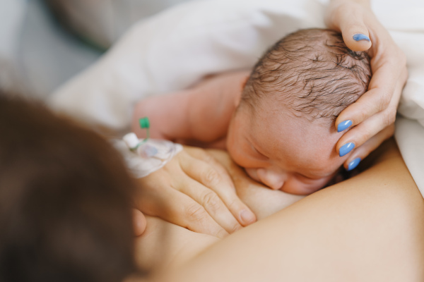 Breastfeeding newborn baby, latching, feeding on first milk, colostrum. Happy mother bonding with newborn baby right after birth. Skin to skin contact.