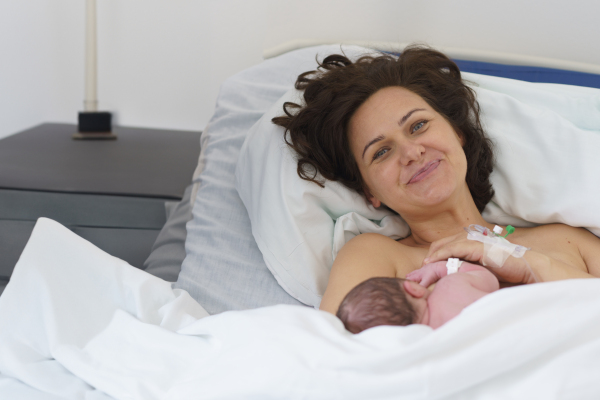 Happy mother bonding with newborn baby right after birth, first latching, breastfeeding. Skin to skin contact.