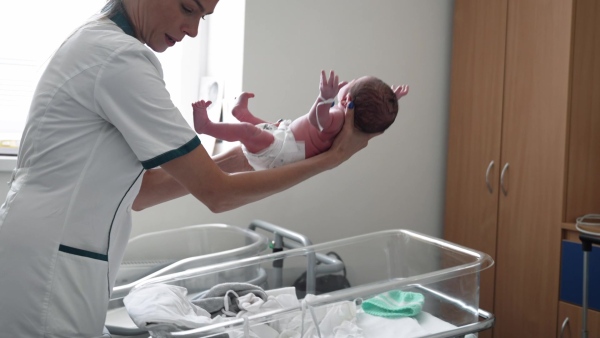 Neonatologist nurse taking care of newborn baby in mothers room. Neonatal care, newborn's health and well-being.