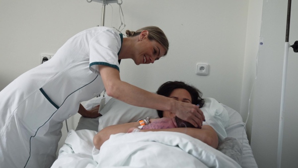 Lactation consultant helping with breastfeeding newborn baby, latching, feeding on first milk, colostrum. Happy mother bonding with newborn baby right after birth. Skin to skin contact.