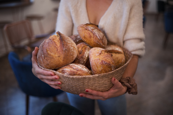 Close-up of woman holding fresh bread in a straw basket.