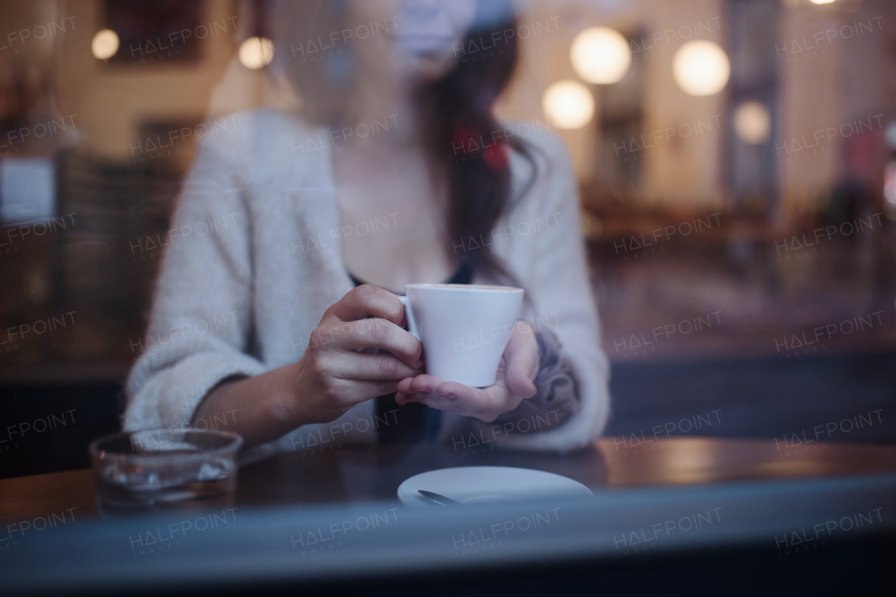 Close-up of woman holding cup of coffee, siting in cafe.