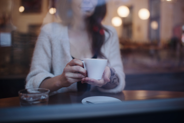 Close-up of woman holding cup of coffee, siting in cafe.