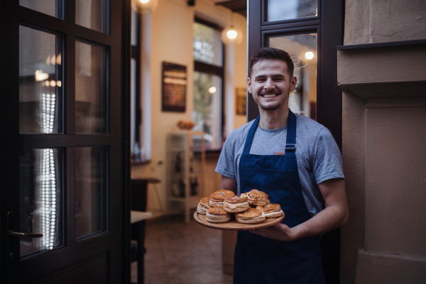 Man with apron holding fresh pastries, standing at the door.