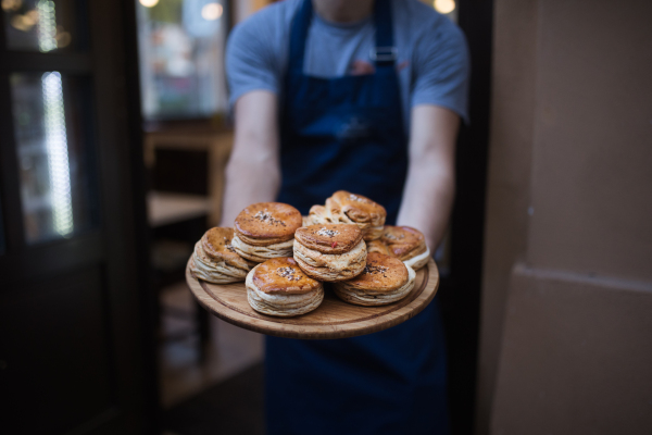 Close-up of man with apron holding fresh pastries, standing at the door.