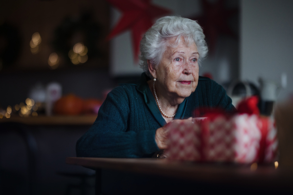 Unhappy senior woman sitting alone and waiting to family during Christmas Eve. Concept of solitude seniors.