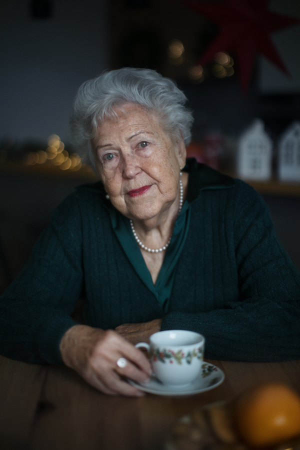 Unhappy senior woman sitting alone and waiting to family during Christmas Eve. Concept of solitude seniors.