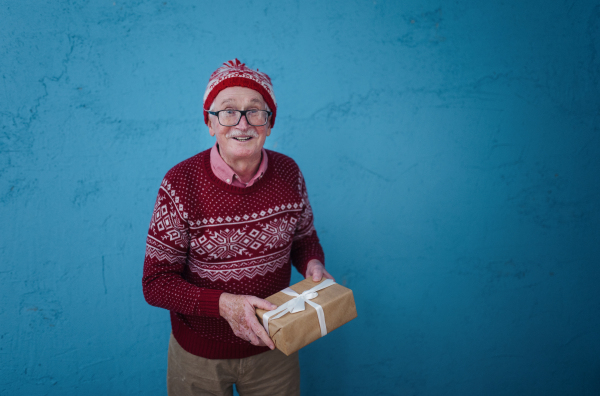 Portrait of happy senior man holding gift, in front of blue background.