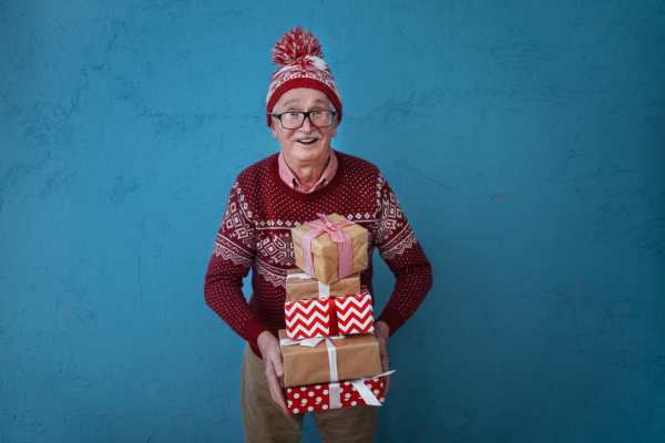 Portrait of happy senior man holding gifts, in front of blue background.