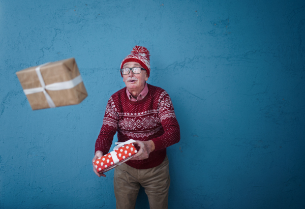 Portrait of happy senior man catching gift, in front of blue background.