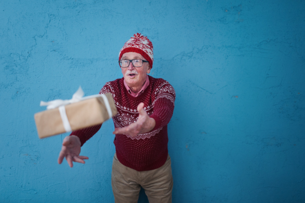 Portrait of happy senior man catching gift, in front of blue background.