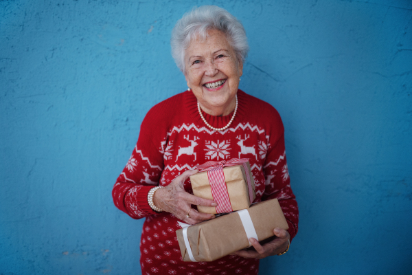 Portrait of happy senior woman holding gift, in front of blue background.