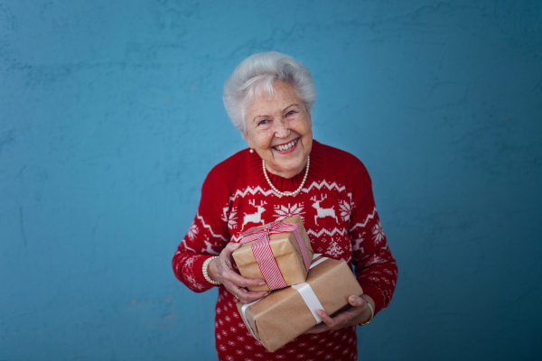 Portrait of happy senior woman holding gift, in front of blue background.