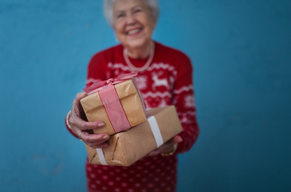 Portrait of happy senior woman holding gift, in front of blue background.