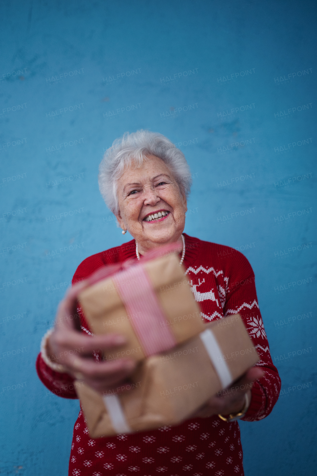 Portrait of happy senior woman holding gift, in front of blue background.