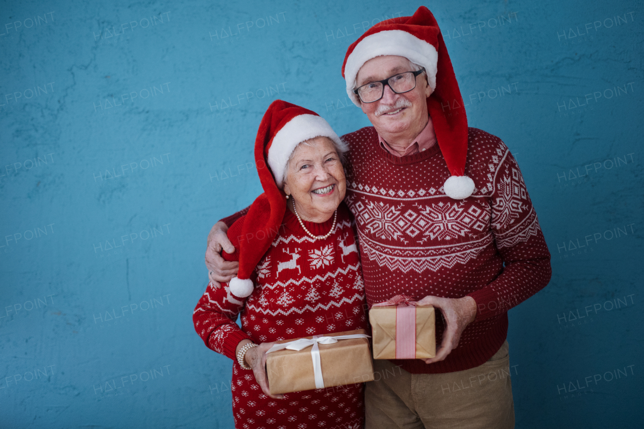 Portrait of happy senior couple holding gifts, in front of blue background.