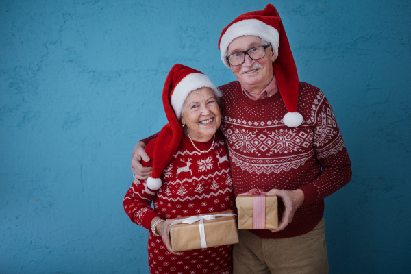 Portrait of happy senior couple holding gifts, in front of blue background.