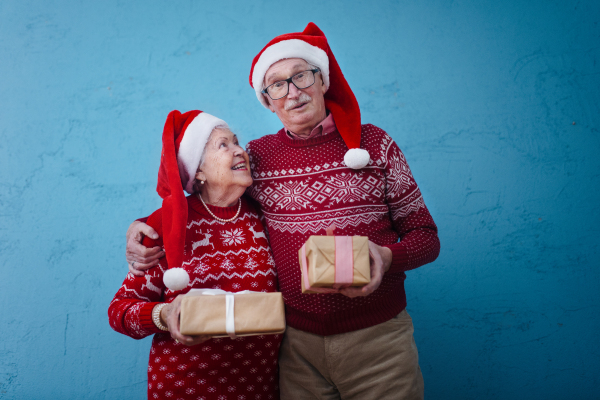 Portrait of happy senior couple holding gifts, in front of blue background.