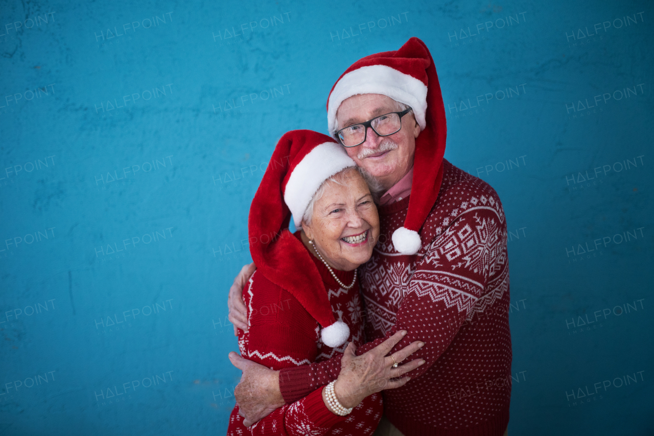 Portrait of happy senior couple in Christmas sweaters hugging,in front of blue background.