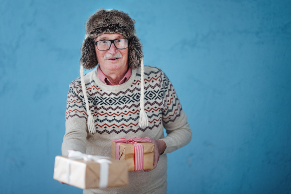 Portrait of happy, excited senior man in warm Chrstimas cap holding gifts.