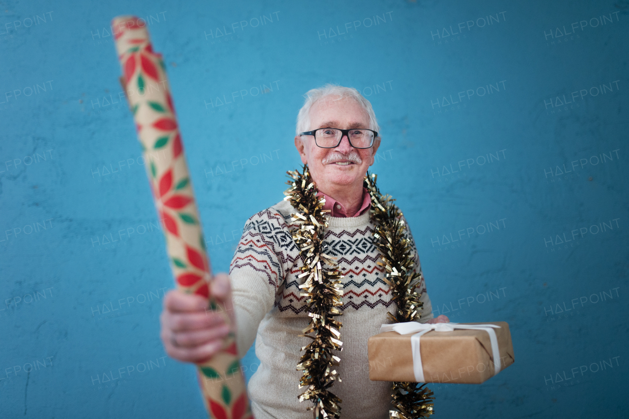 Portrait of happy senior man holding a Christmas gift and wrapping paper studio shooting.