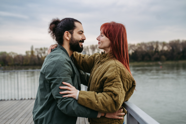 Beautiful couple on romantic date, standing on boardwalk by the river, looking at each other into eyes