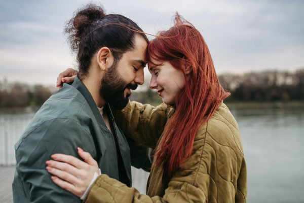 Beautiful couple on romantic date, standing on boardwalk by the river, touching with foreheads