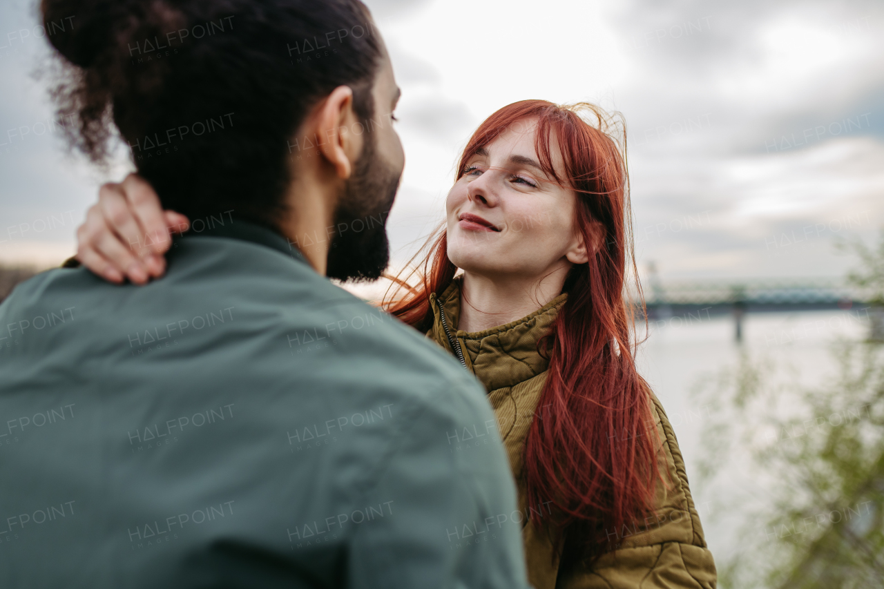 Beautiful couple on romantic date, standing on boardwalk by the river, looking at each other into eyes