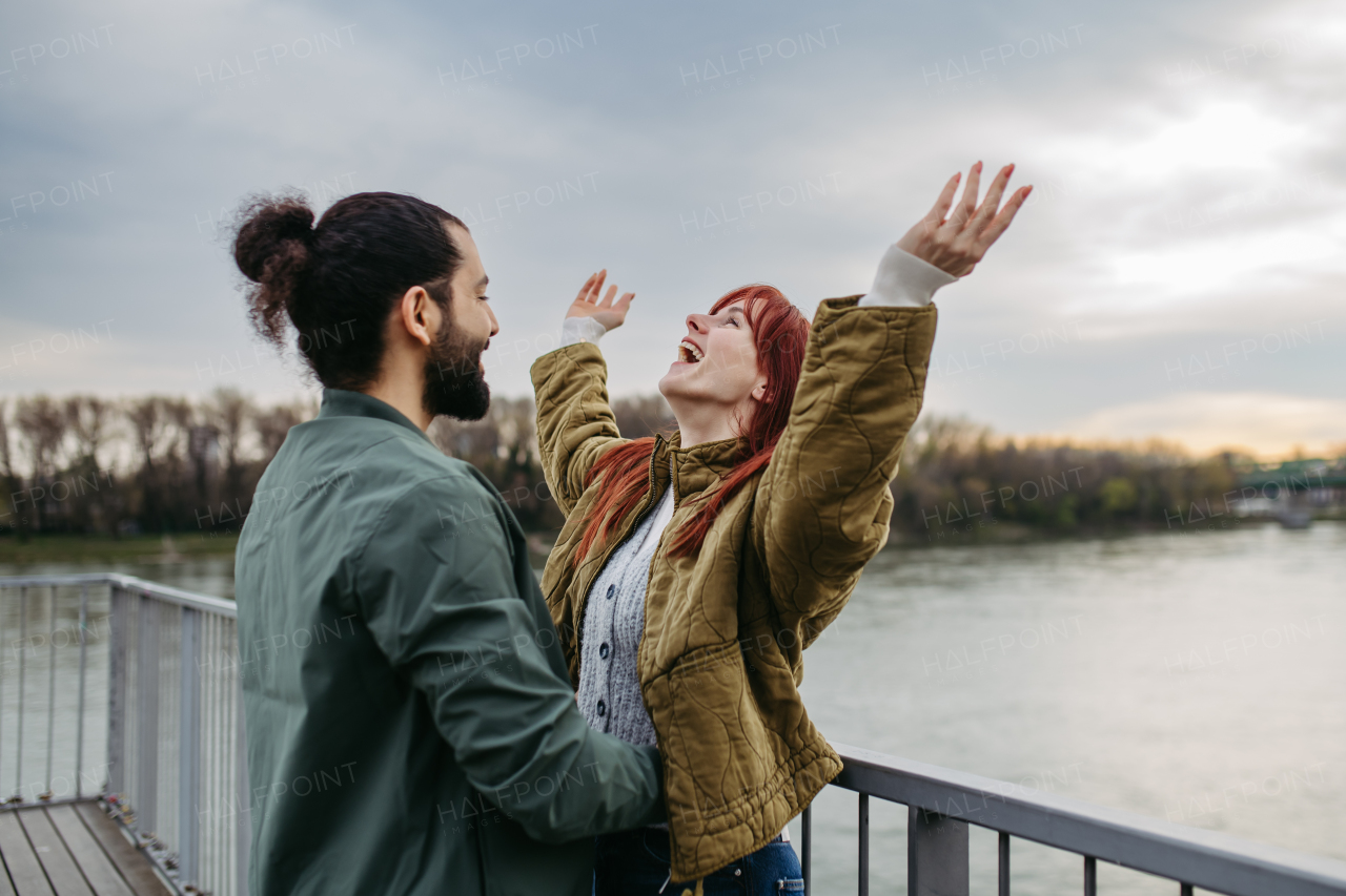 Beautiful couple on romantic date in the city, standing on boardwalk by the river. Hands up in the air.