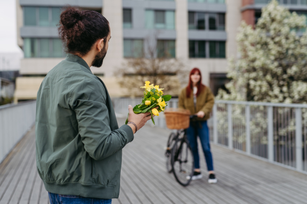 Couple on date in the city, meeting on the street. Man brings flowers for his girlfriend. Romantic date during cold spring day