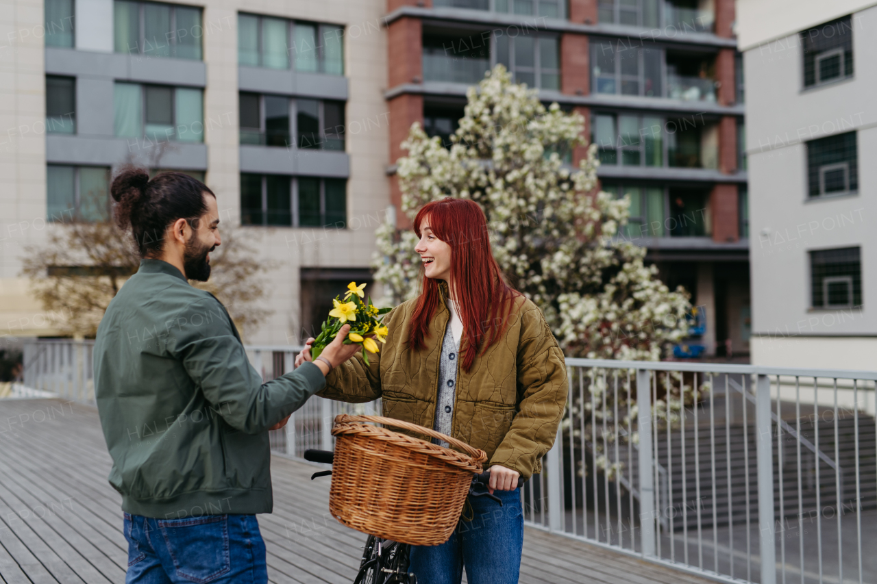 Couple on date in the city, meeting on the street. Man brings flowers for his girlfriend. Romantic date during cold spring day