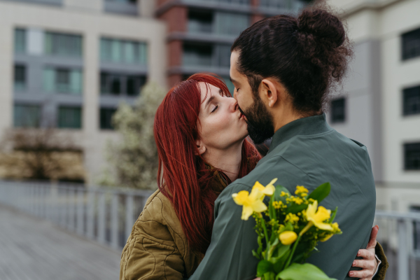 Girlfriend and boyfriend meeting in the city, greeting each other with hug and kiss. Romantic date during cold spring day.