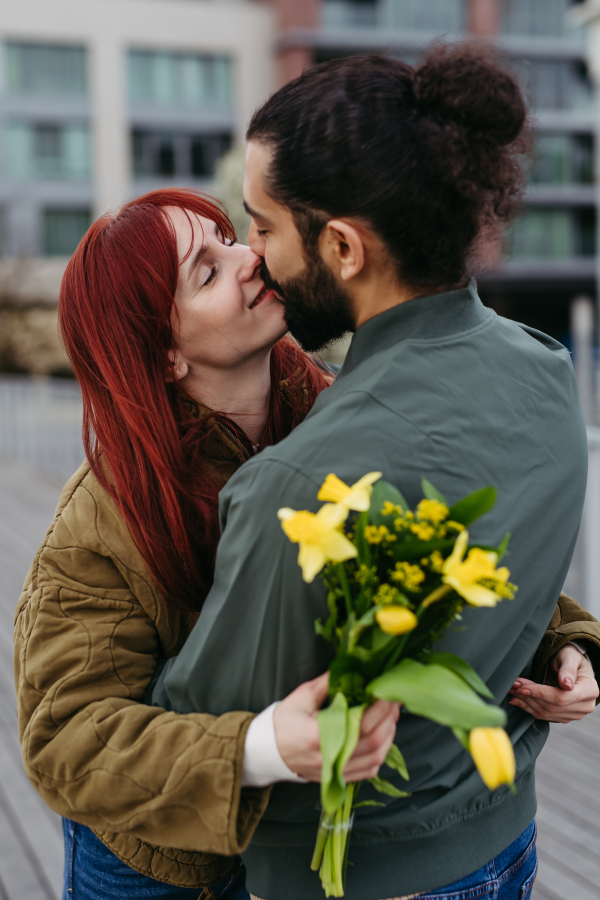 Girlfriend and boyfriend meeting in the city, greeting each other with hug and kiss. Romantic date during cold spring day.