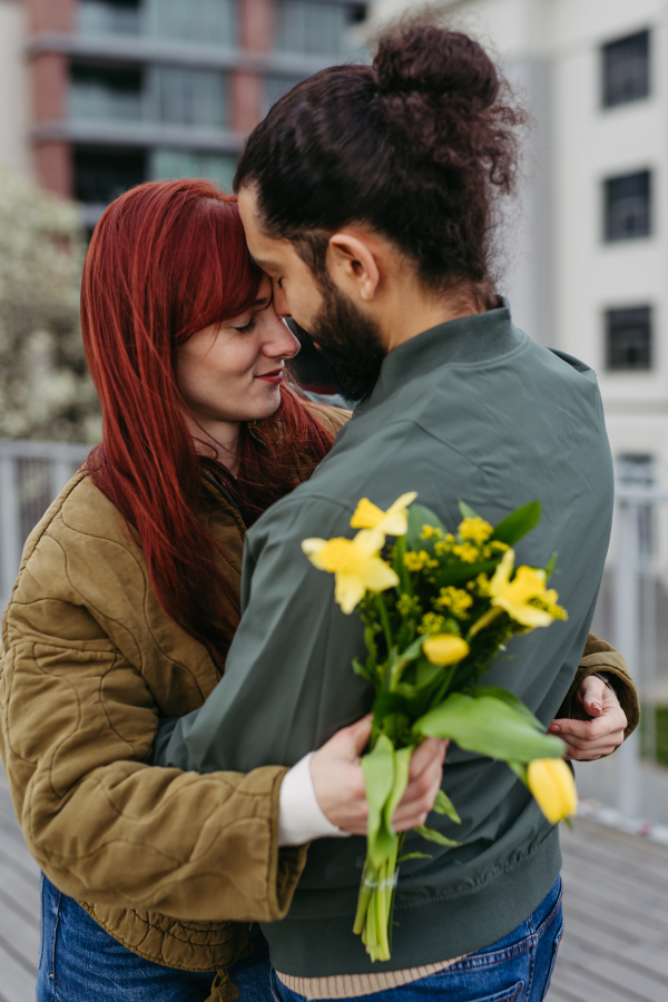 Girlfriend and boyfriend meeting in the city, greeting each other with hug, touching with foreheads. Romantic date during cold spring day