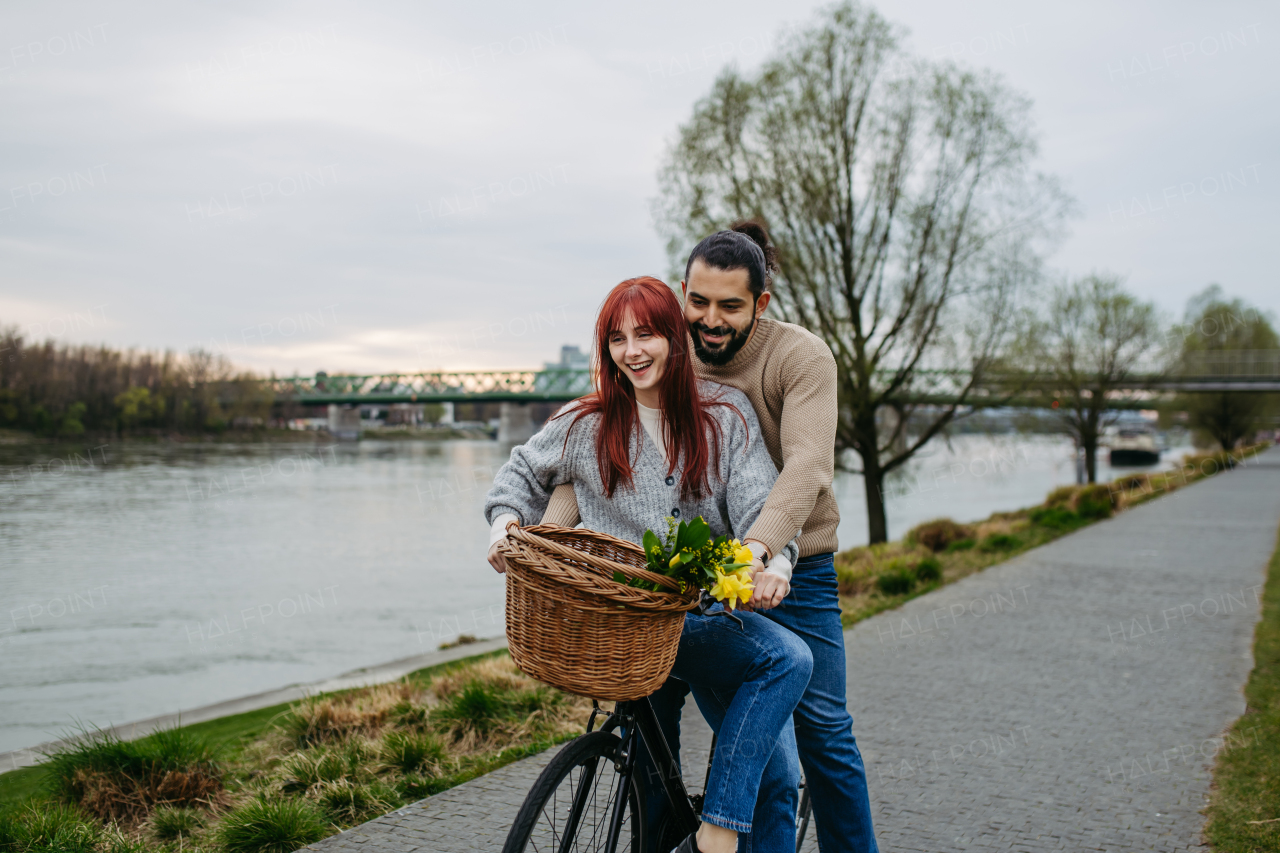 Boyfriend giving ride to his girlfriend on bicycle, sitting on frame. Beautiful couple on romantic date during cold spring or autumn day.